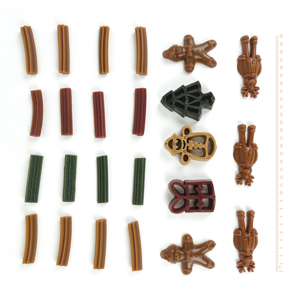 Assorted vegetable based dog snack items from the doggie christmas advent calendar including snowman, gingerbread man, reindeer, christmas tree on a white background with a ruler for scale.