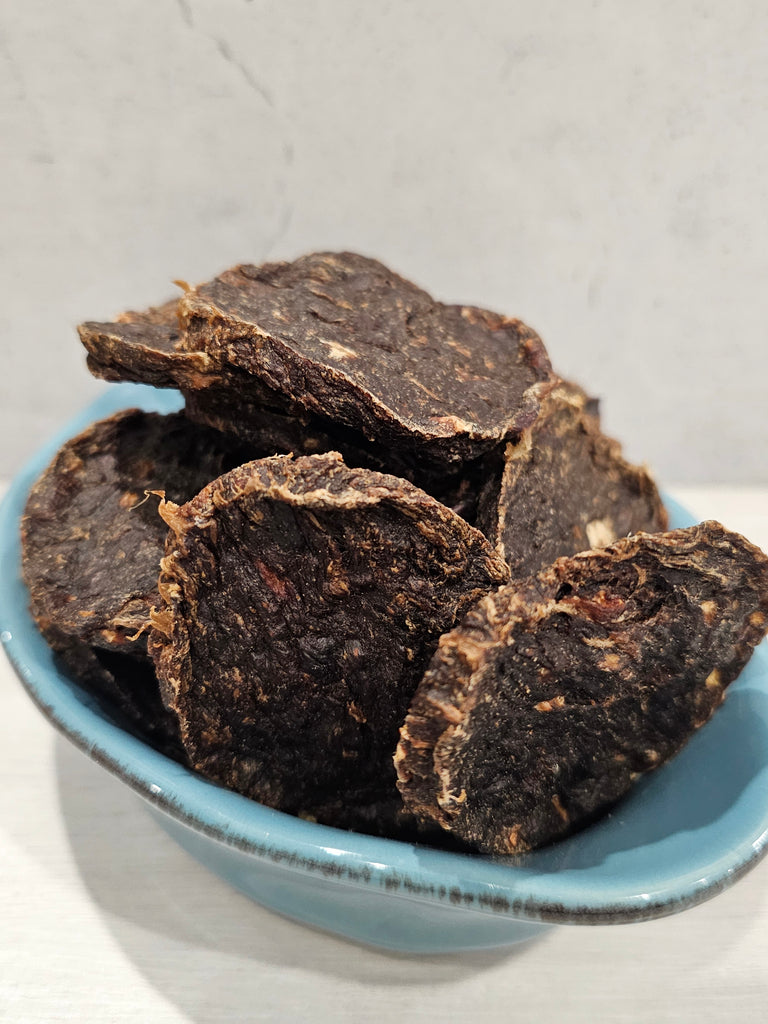 Dehydrated roo and rabbit patties for dogs in a blue bowl on a light gray background