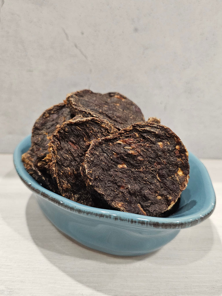 Close up of Dehydrated roo and rabbit patties for dogs in a blue bowl on a light gray background